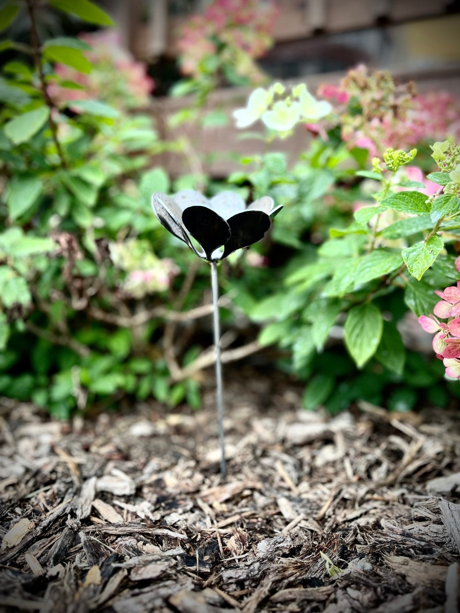 Butterfly-shaped garden stake in a garden setting with blurred flowers in the background. Henderson Garden Supply