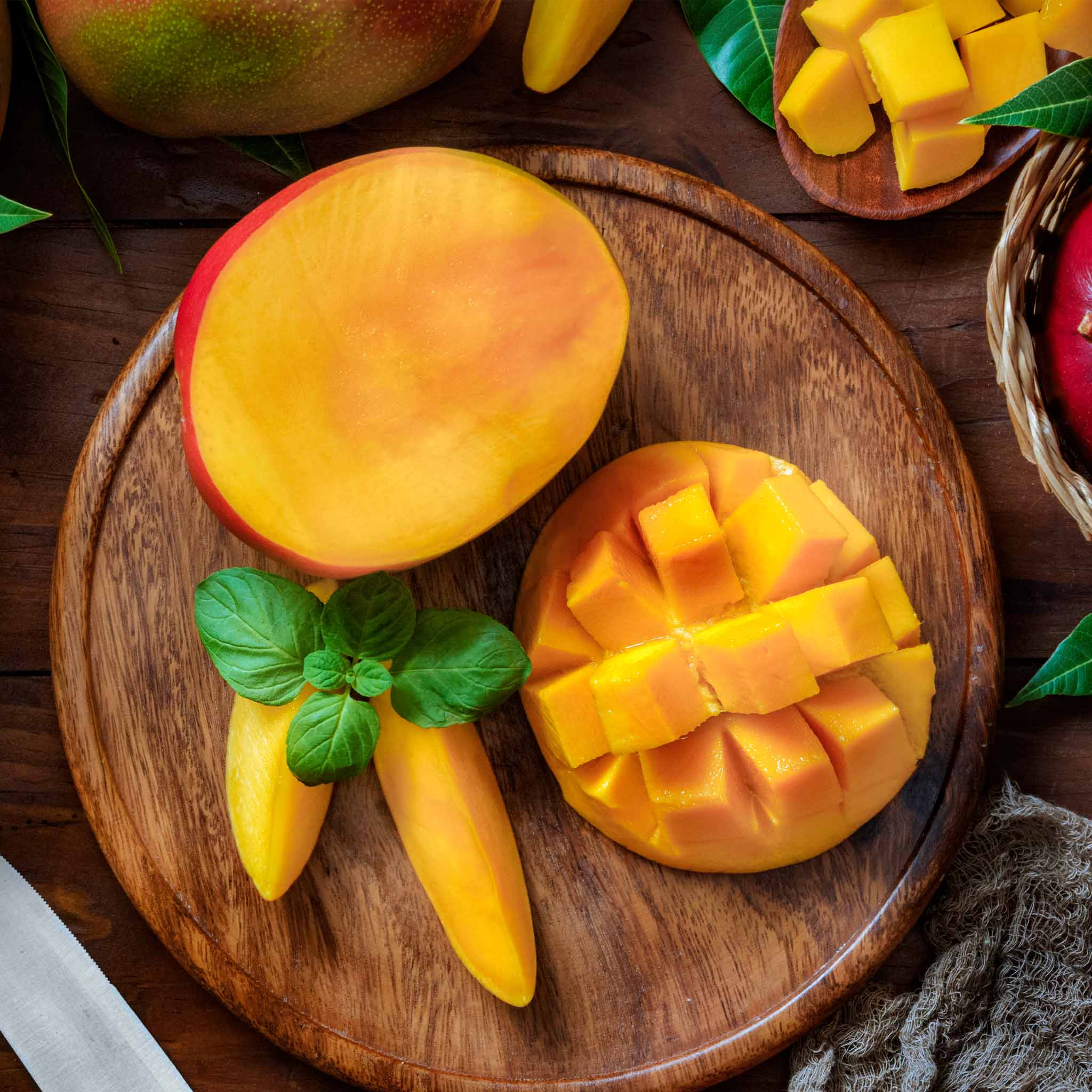 Sliced mango on a wooden cutting board with whole mangoes and a knife in the background. Henderson Garden Supply