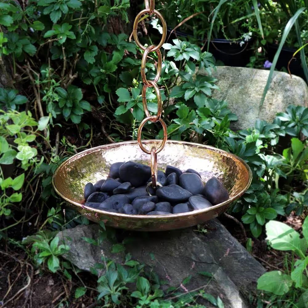 Copper rain chain with a bowl of black stones in a garden setting. Henderson Garden Supply