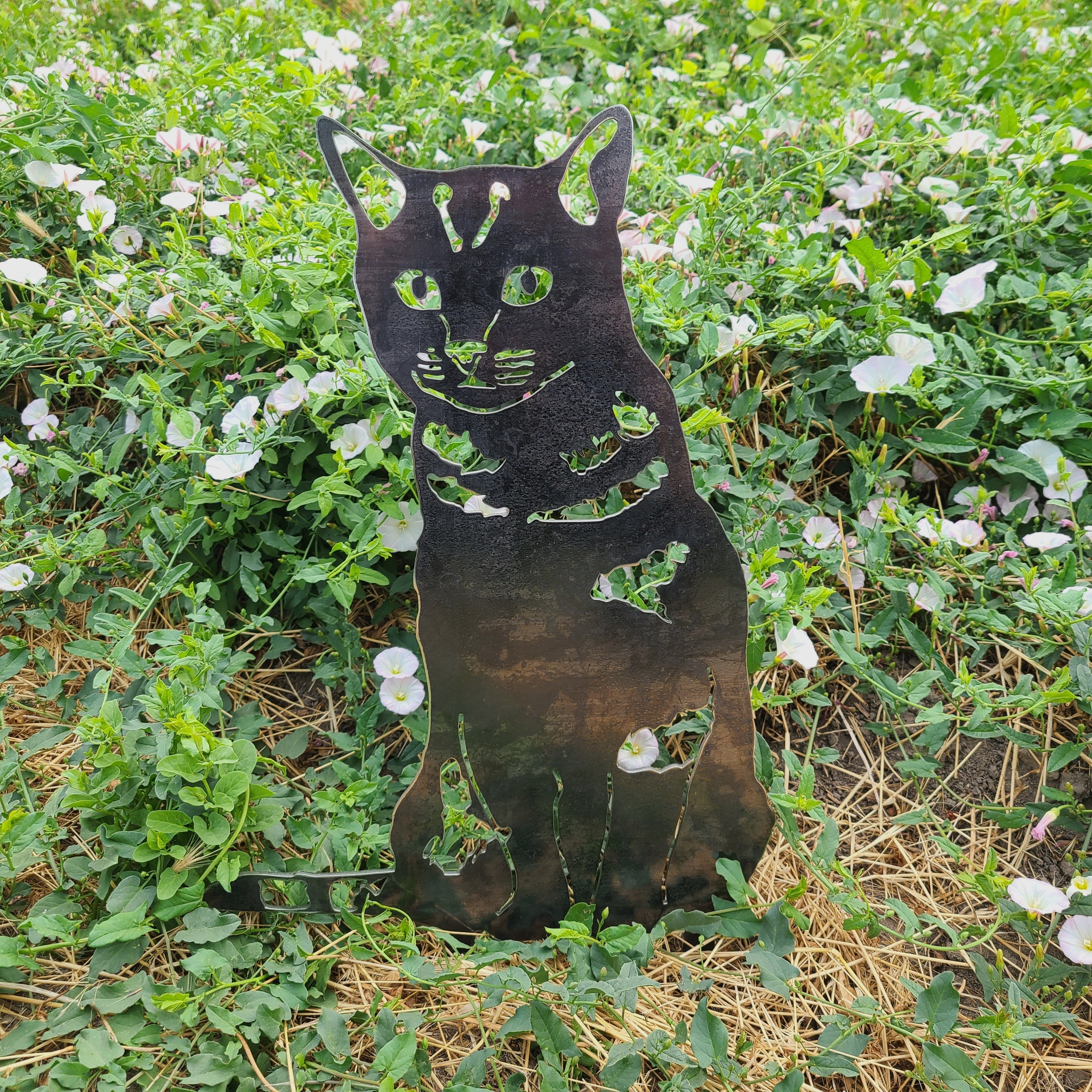 Metal cat sculpture in a garden with green grass and white flowers. Henderson Garden Supply