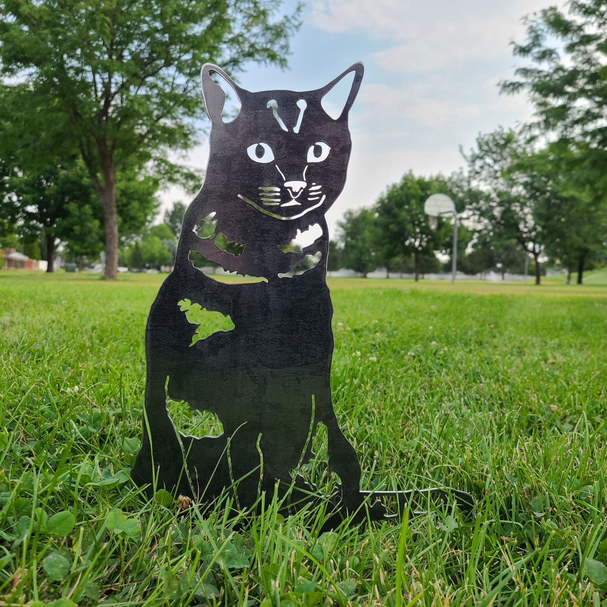 Black cat-shaped metal object on grass with trees and sky in the background. Henderson Garden Supply