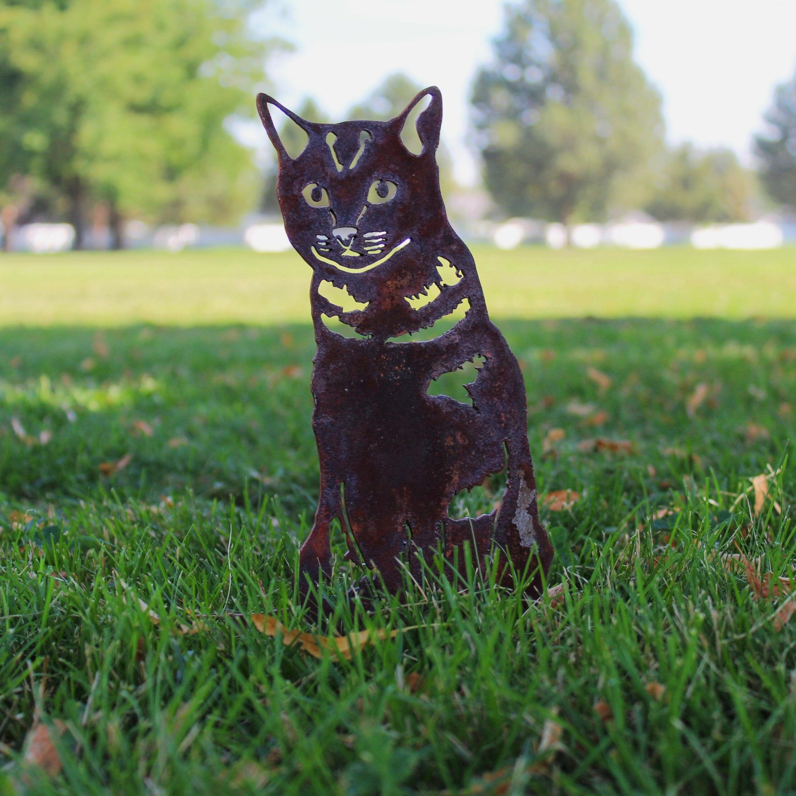 Metallic cat sculpture on grass with trees in the background. Henderson Garden Supply