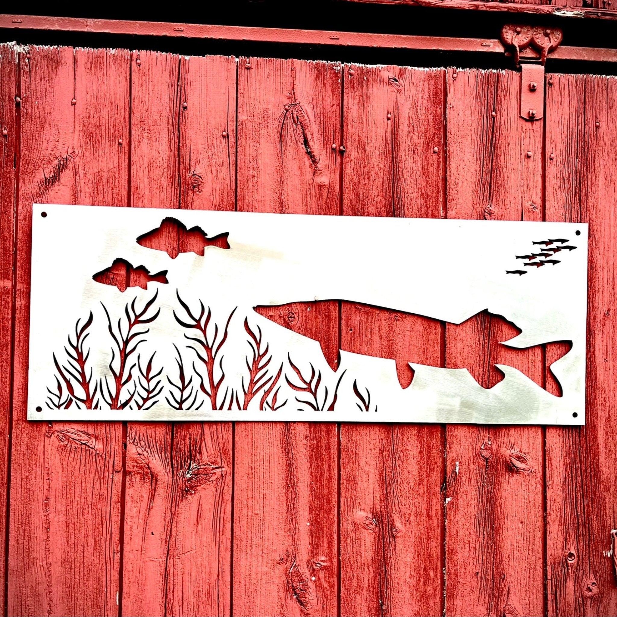 Decorative metal sign with fish design on a red wooden background. Henderson Garden Supply