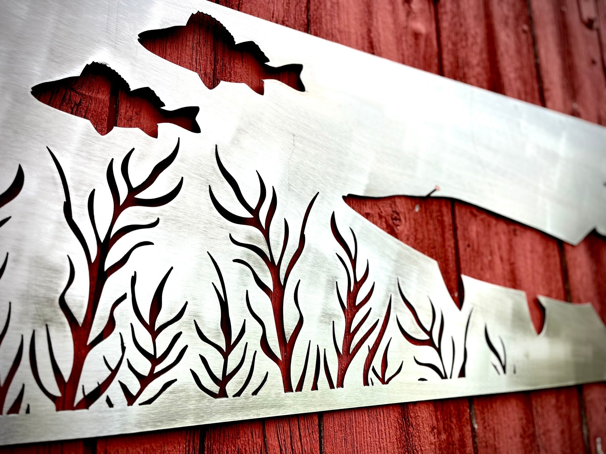 Metal wall art with fish and trees on a red wooden background. Henderson Garden Supply