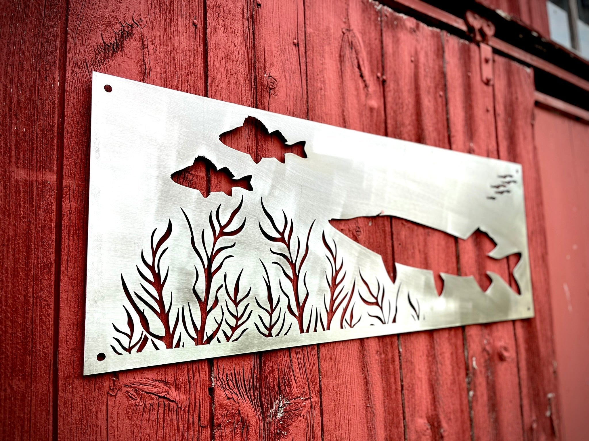 Metal decorative panel with fish and seaweed design on a red wooden background. Henderson Garden Supply