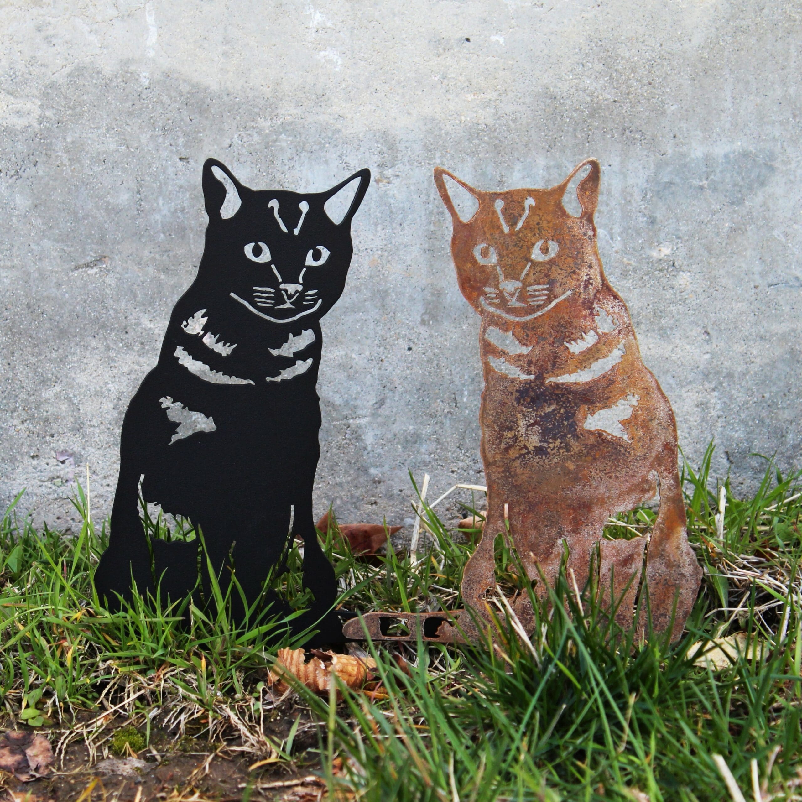 Metallic black and copper cat sculptures on grass against a concrete wall.  Henderson Garden Supply