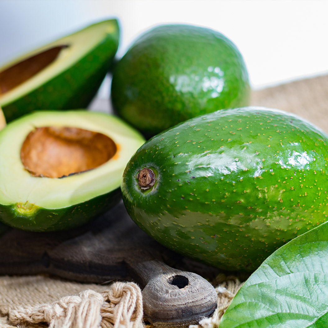 Avocados with one cut open on a rustic surface.  Henderson Garden Supply