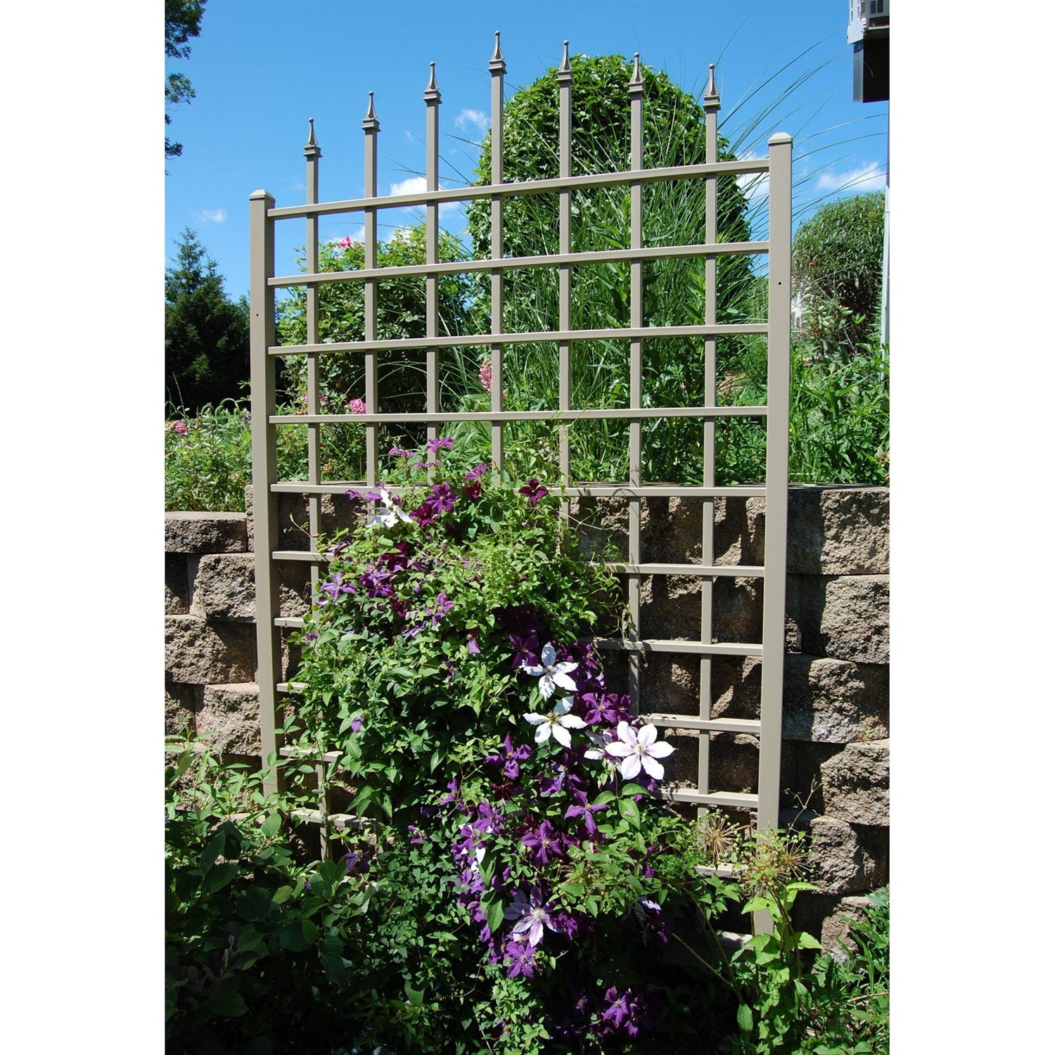 Garden trellis with climbing plants and flowers against a stone wall and blue sky.  Henderson Garden Supply