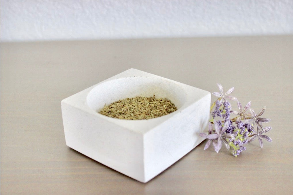 White ceramic bowl with dried herbs on a beige surface.  Henderson Garden Supply
