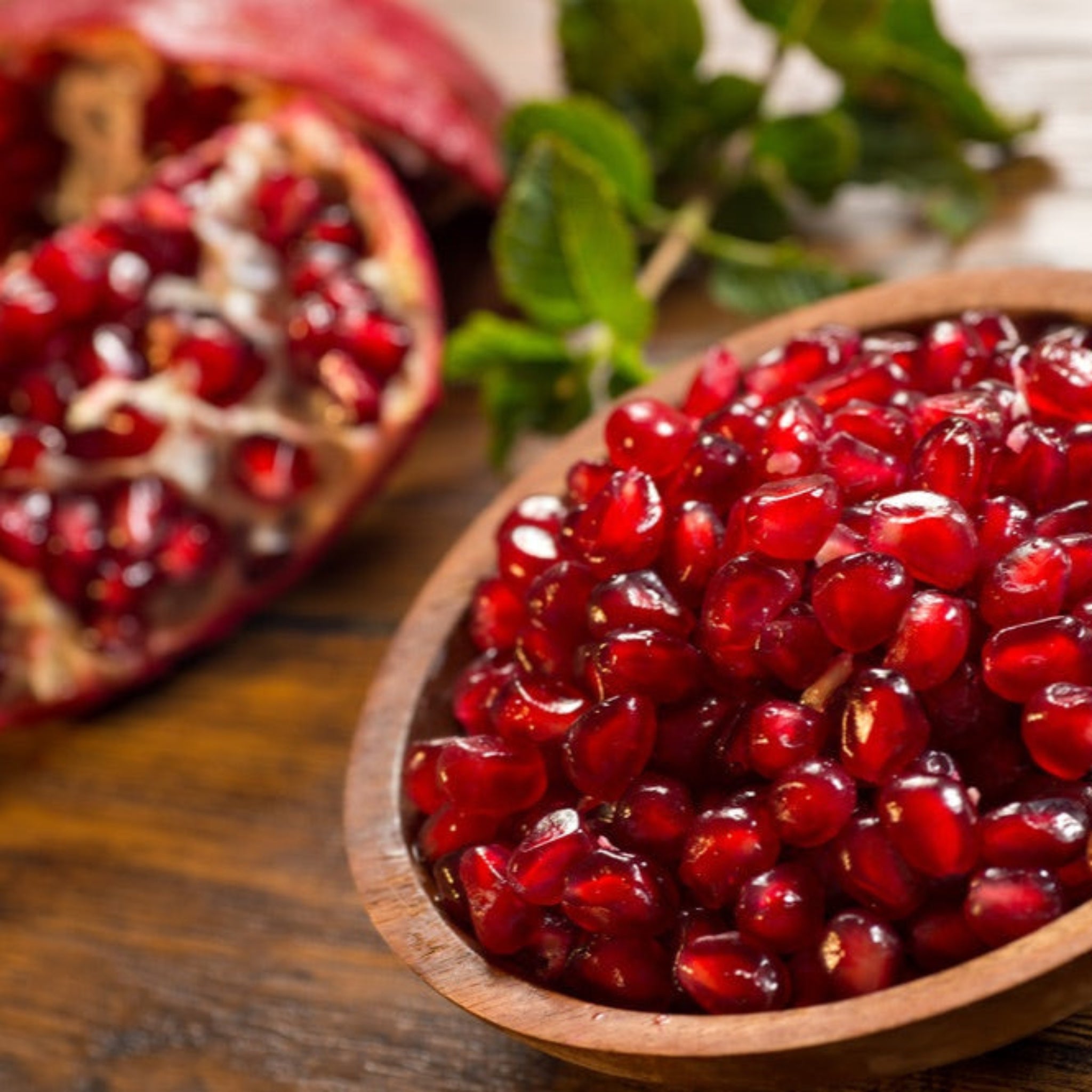 Pomegranate seeds in a wooden bowl with a whole pomegranate in the background.  Henderson Garden Supply