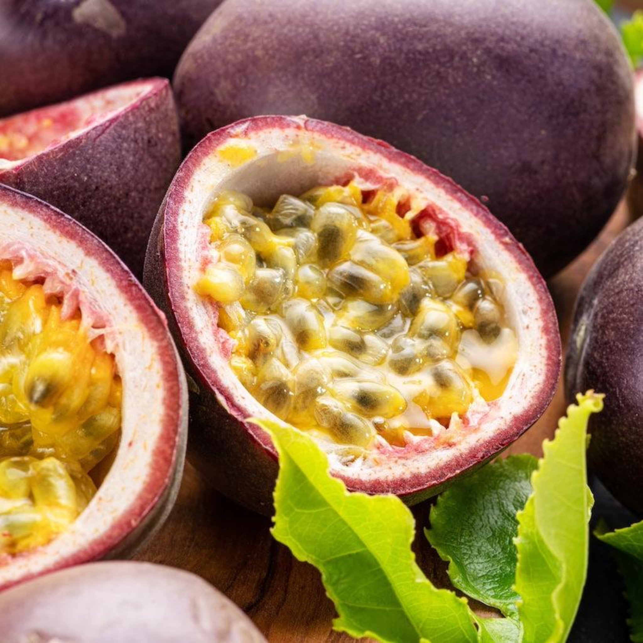 Close-up of a halved passion fruit with seeds and a green leaf on a wooden surface.  Henderson Garden Supply