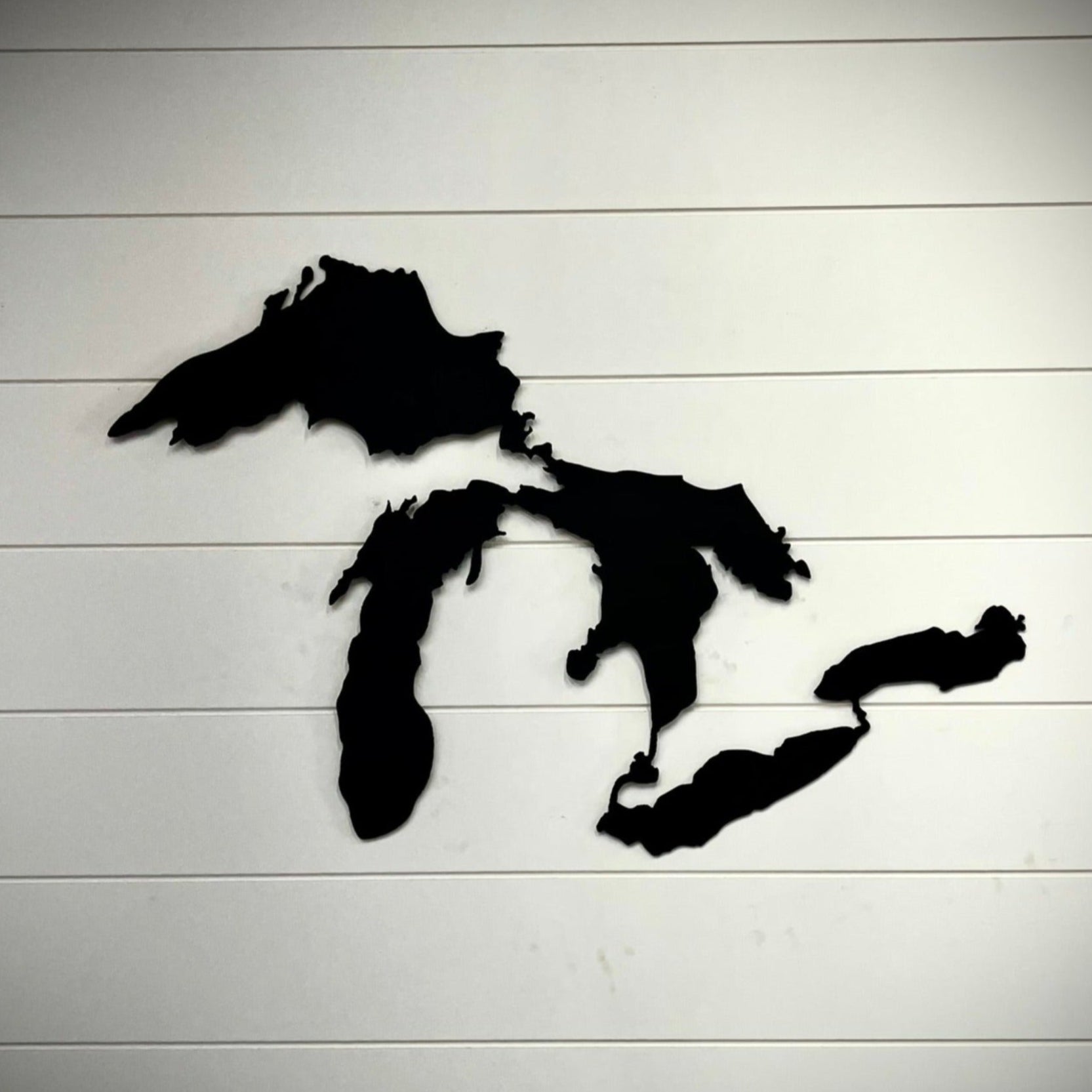 Black silhouette of the Great Lakes on a white wooden background.  Henderson Garden Supply