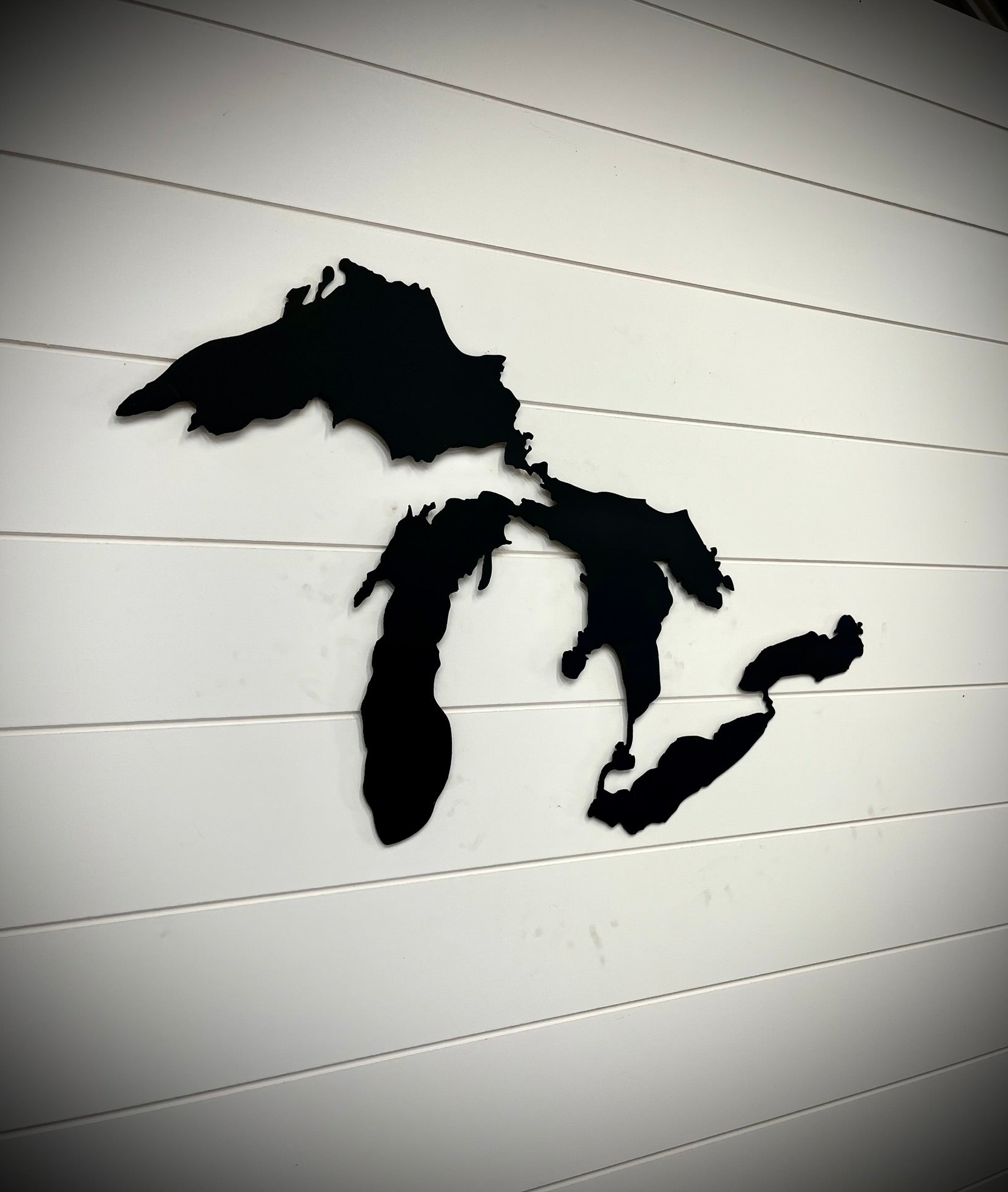 Black silhouette of the Great Lakes on a white wooden background.  Henderson Garden Supply