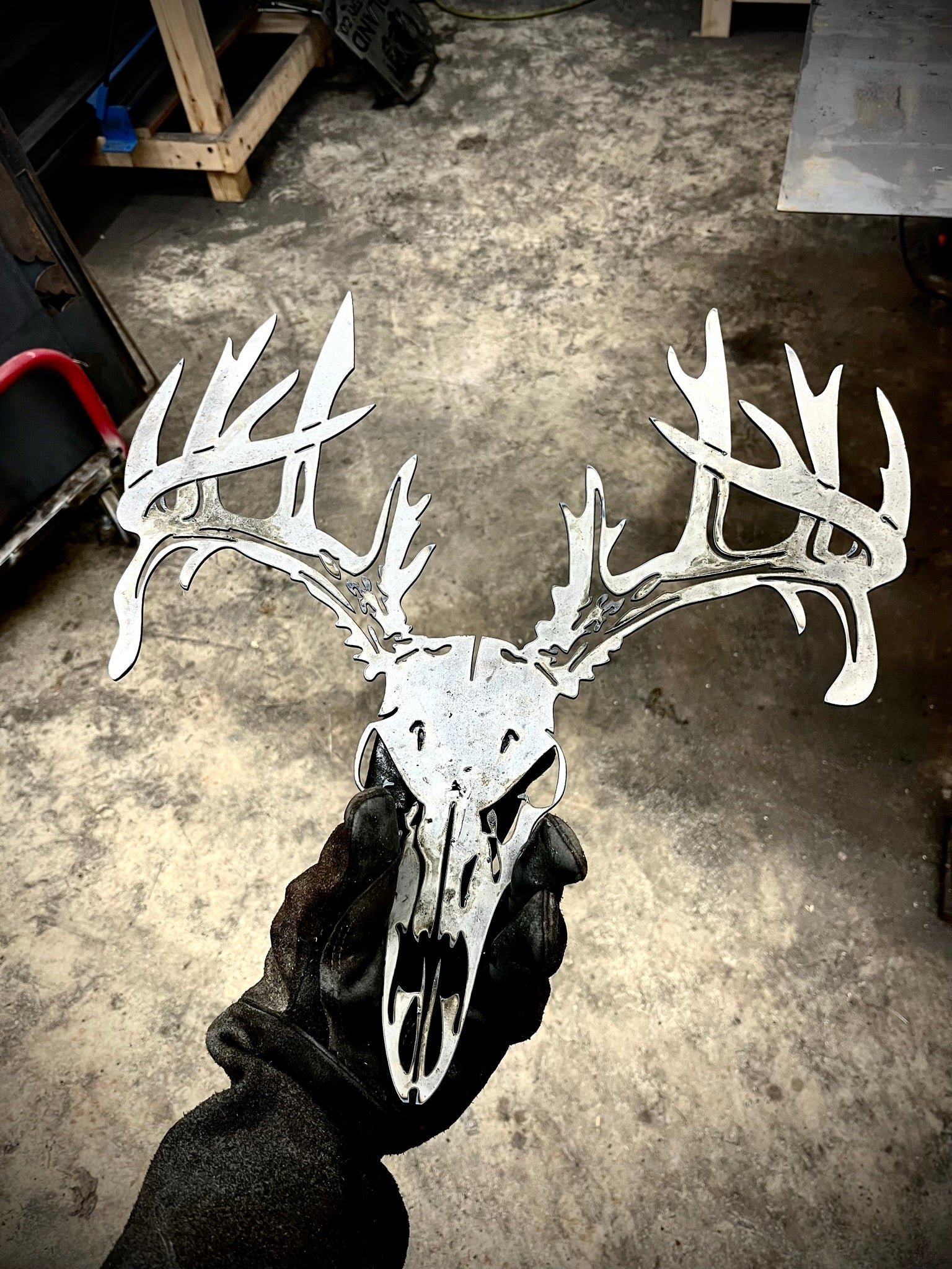 Metallic deer skull with antlers held by a gloved hand on a concrete floor. - Henderson Garden Supply