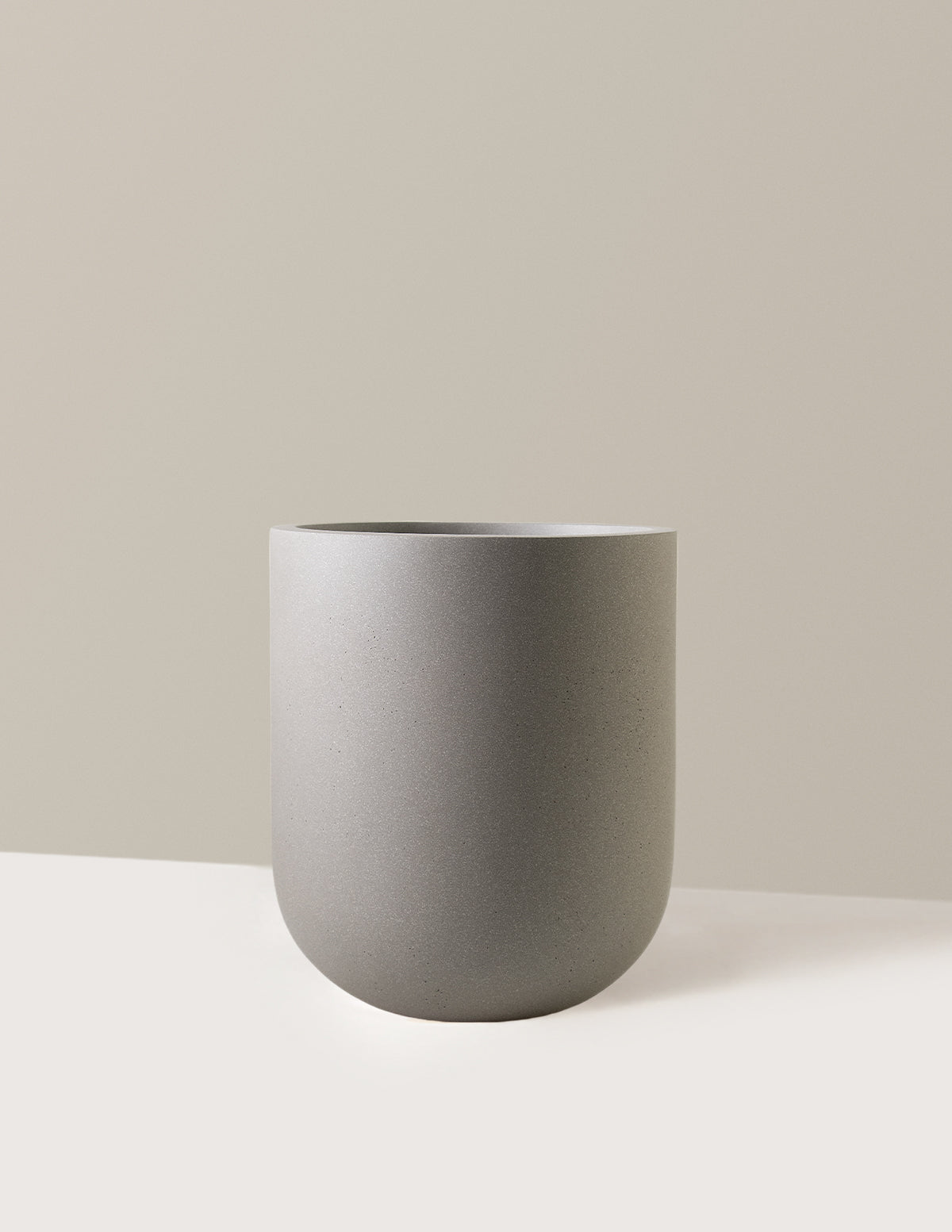 Gray ceramic planter on a white surface with a beige background.  Henderson Garden Supply